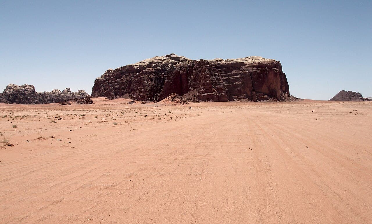 Vidstrakt rød ørken med oppstikkende sandsteinsfjell i Wadi Rum